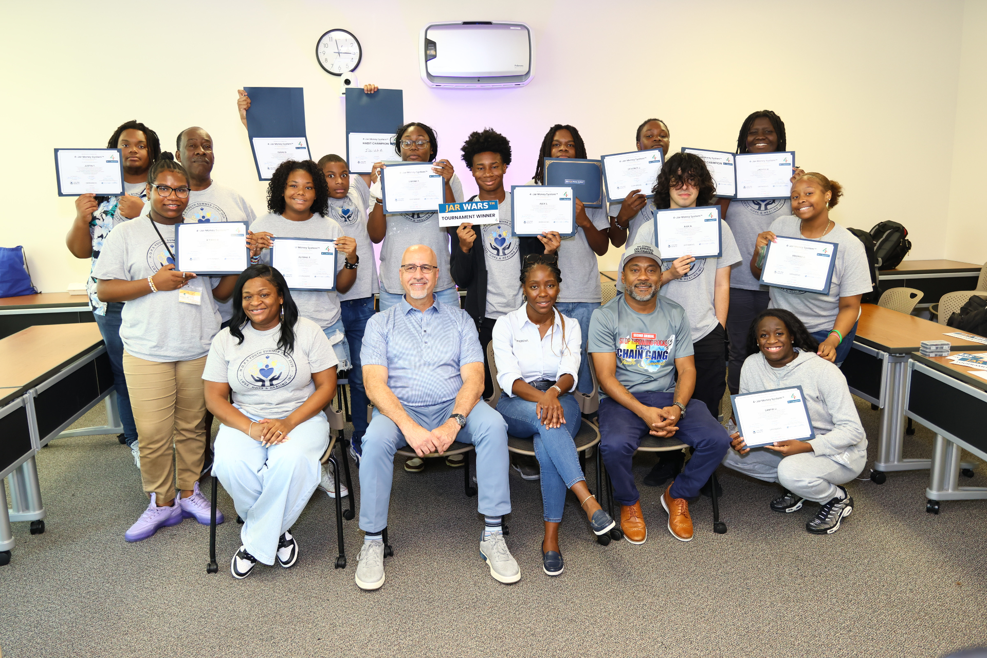 Youth cohort holding 4-Jar Money System™ certificates alongside program facilitators